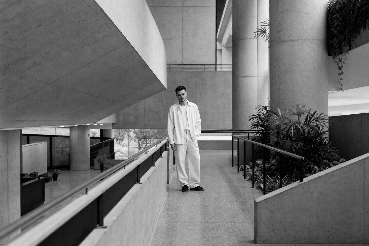 Matheus Meira em uma passarela de concreto de arquitetura modernista, fotografado em preto e branco